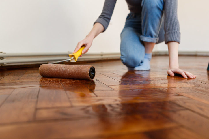 a person trying to refinish their hardwood floors by hand & DYI